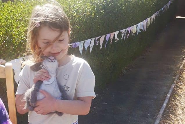 Phoebe, 6, giving a teddy a squeeze in front of some colourful bunting