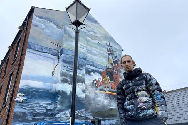 Artist Lewis Hobson with the lifeboat mural he is painting on the side of the Ship Inn on the Headland. Picture by FRANK REID