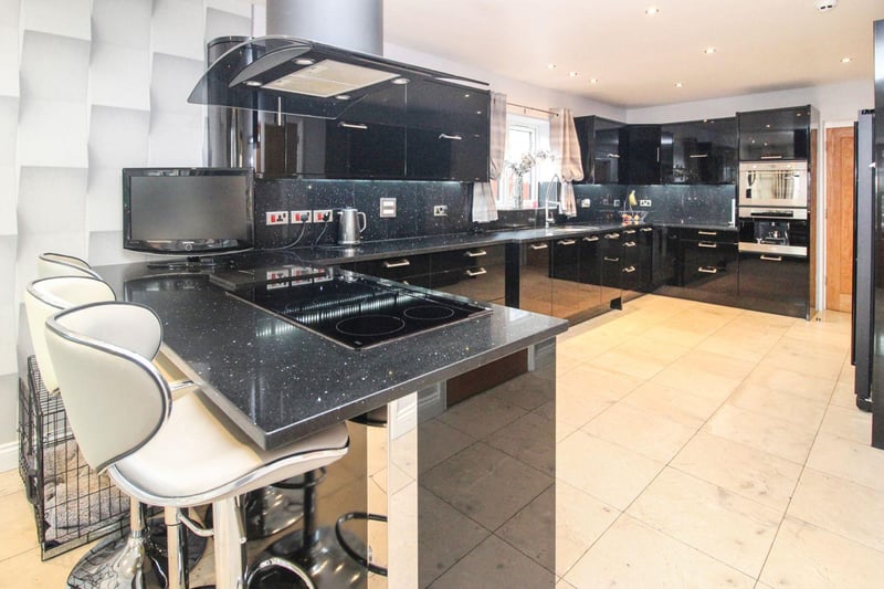 The kitchen is modern in style and is fitted with contemporary high gloss wall and base units, a double over, breakfast bar with integrated electric hob, and marble tiled flooring.