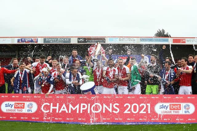 Ben Tozer of Cheltenham Town lifts the Sky Bet League Two Trophy as his team mates celebrate after the Sky Bet League Two match between Cheltenham Town and Harrogate Town at The Jonny-Rocks Stadium on May 08, 202 (Photo by Matthew Lewis/Getty Images)