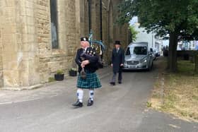 A Scottish piper leads the hearse to the funeral service.