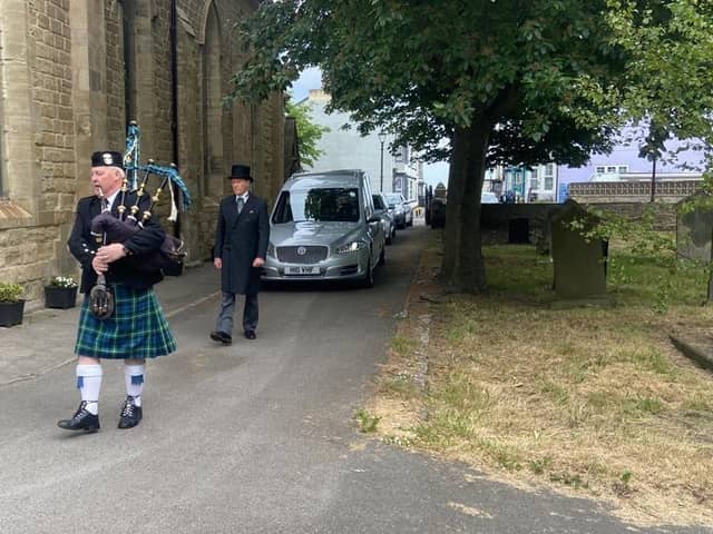 A Scottish piper leads the hearse to the funeral service.