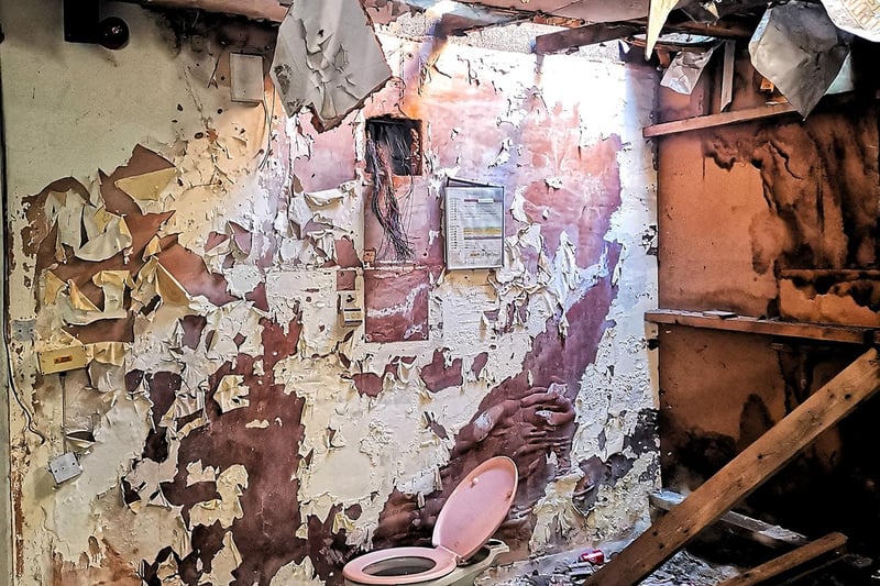 Paint is peeling from the walls in this room, in which an old toilet sits