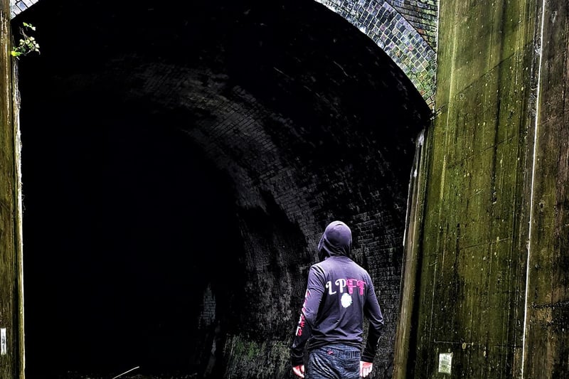 An urban explorer stands at the tunnel mouth.