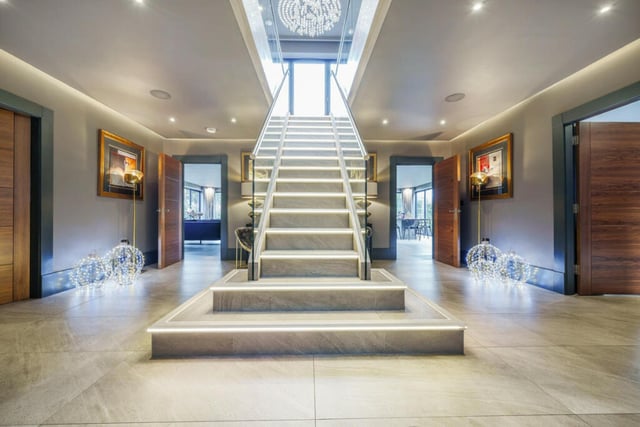 This home has an extravagant entrance hall featuring porcelain steps, a glass banister and seating area beneath the staircase.