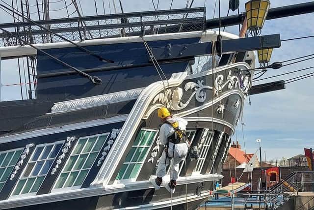 Workers are secured by harnesses as they paint the vessel.