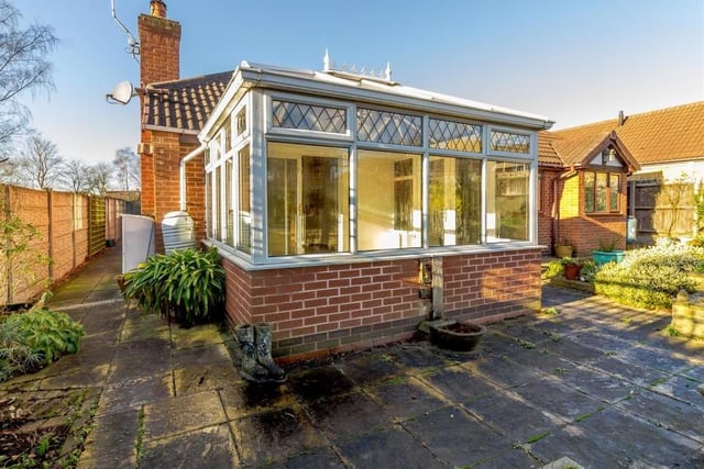 This shot from the back garden shows the conservatory and the extensive, paved path at the side of the bungalow that offers space for wheelie-bin storage. A large, paved patio extends the full width of the property.