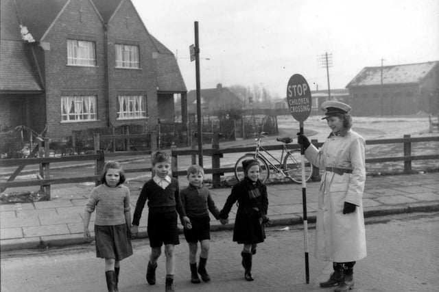 A lollipop lady stops the traffic to allow four youngsters to cross the road safely near the Owton Lodge.