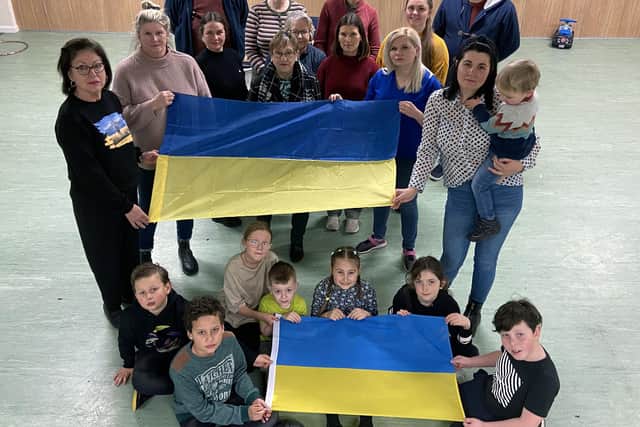 Fiona Cook community engagement manager with the Big League (left) and Irina Tykhoneko from the Ukraine hold the Ukrainian flag as members of the “Big League Community  gather round. Picture by FRANK REID
