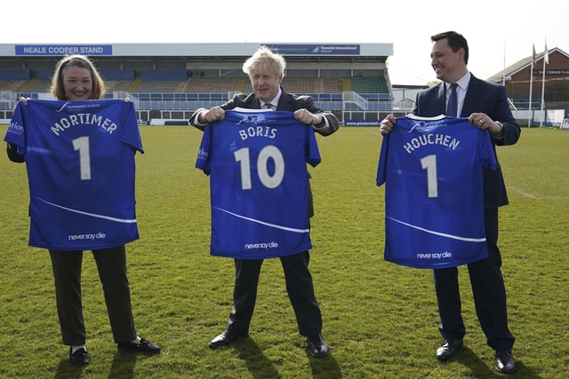 Jill Mortimer, Conservative party candidate for Hartlepool, Britain's Prime Minister Boris Johnson, and Ben Houchen, Tees Valley Mayor, from left,  are presented with personalized Hartlepool United soccer team shirts in 2021. Photo: Ian Forsyth/Pool via AP.