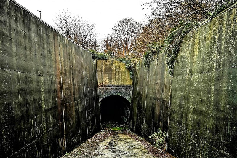 A concrete ramp, hemmed in on both sides by concrete walls, leads to the tunnel entrance.