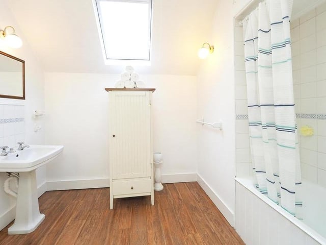 The family bathroom is fitted with a three-piece suite, made up of a panelled bath with wall-mounted mixer tap and rainfall shower overhead, low-level WC and pedestal wash hand basin. The floor is laminated, lights adorn the wall and a Velux roof light adds to the brightness.