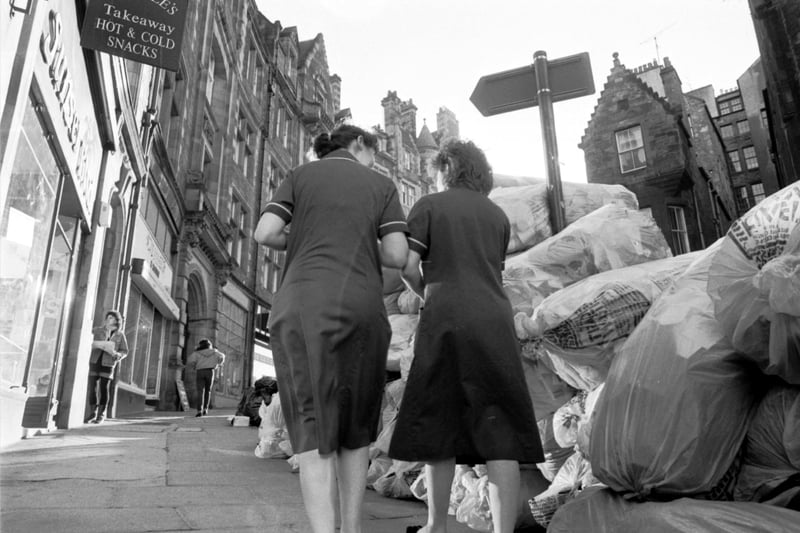 Nurses walk past plastic bags full of rubbish piled up on the pavement in Cockburn Street Edinburgh during the bin men's strike in November 1987.