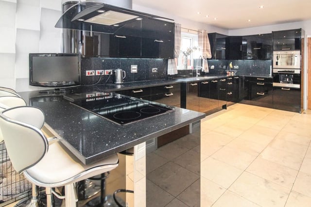 The kitchen is modern in style and is fitted with contemporary high gloss wall and base units, a double over, breakfast bar with integrated electric hob, and marble tiled flooring.