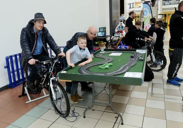 Tony Davison (right) (sustainable travel officer) and Tyler Richardson look on as Tyler's dad Gareth rides the bike that powers the Scalextric track. Picture by FRANK REID
