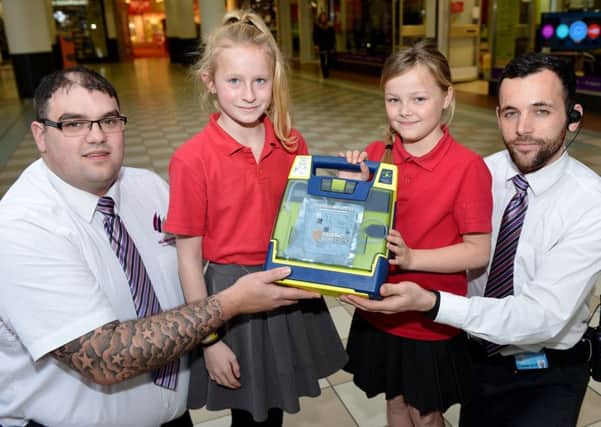 Middleton Grange Shopping centre security supervisors Paul Foster (left) and Adam Goodwin present a defibrillator to Stranton Primary School pupils Eden Popryez (left) and Skye Lynn. Picture by FRANK REID