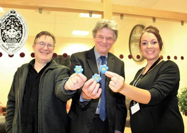 Hartlepool resident Eric Hughes who is living well with dementia, Hospital of God Director David Granath, and manager of The Bridge Laura Robinson show their support for dementia with Alzheimers Society forget-me-not flowers