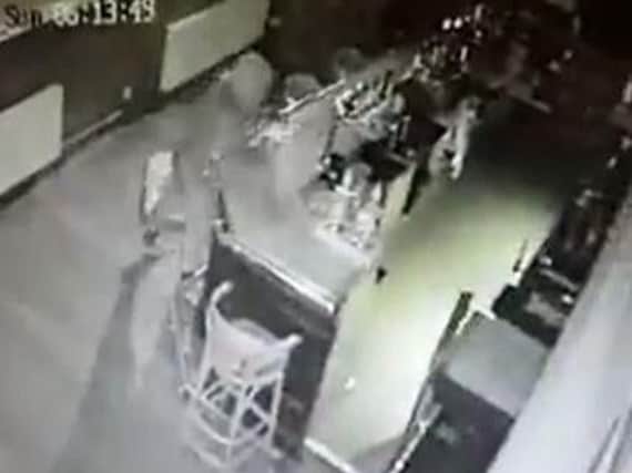 One of the intruders snatches a tin from the bar of The Causeway.